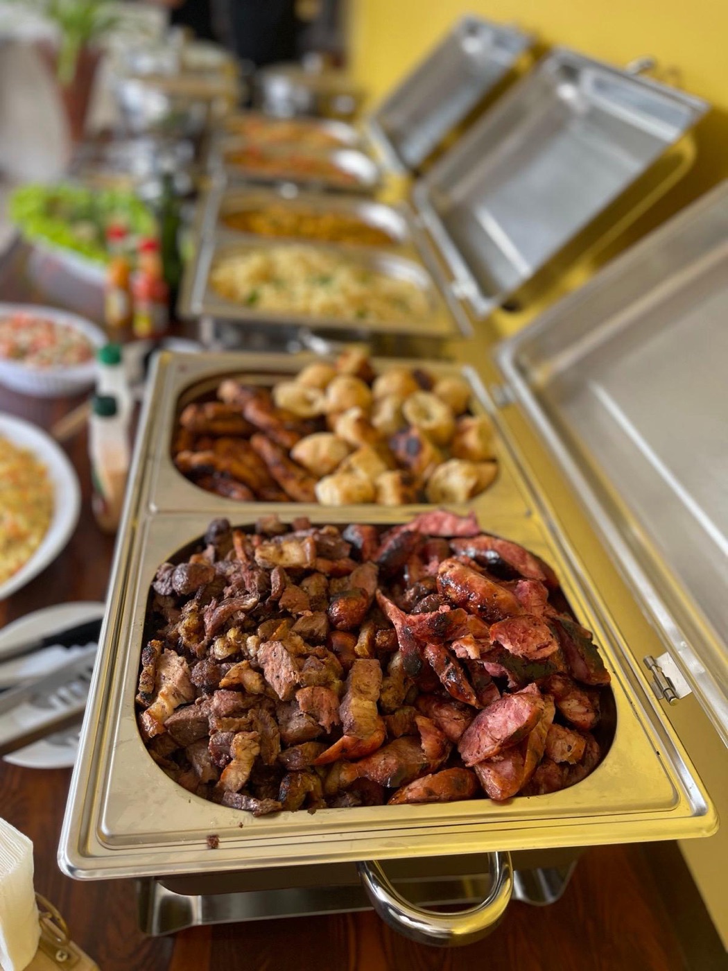 Fila de rechauds com carnes, pão de alho e acompanhamentos